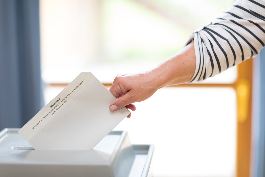 Eine Person, die ihren Wahlzettel in eine Abstimmungsurne einwirft.