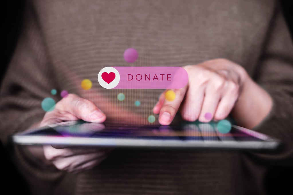 A person using a tablet with a colorful 'DONATE' button displayed on the screen.